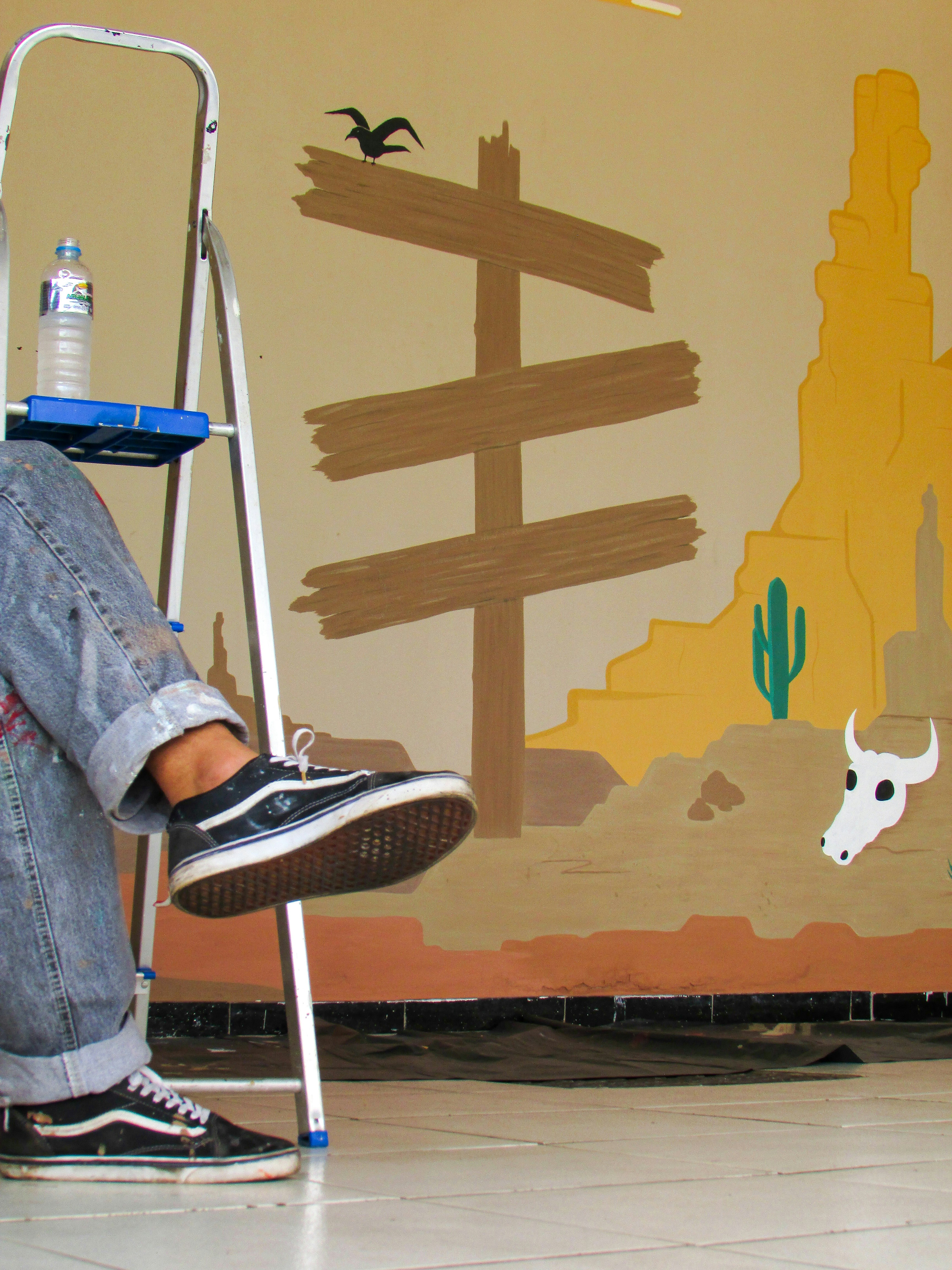 a man sitting on a step ladder painting a mural