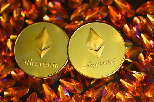 Two gold coins featuring the Ethereum logo are surrounded by numerous shiny, orange gemstones on a dark background. The coins have the Ethereum symbol and the word 'Ethereum' embossed on them.