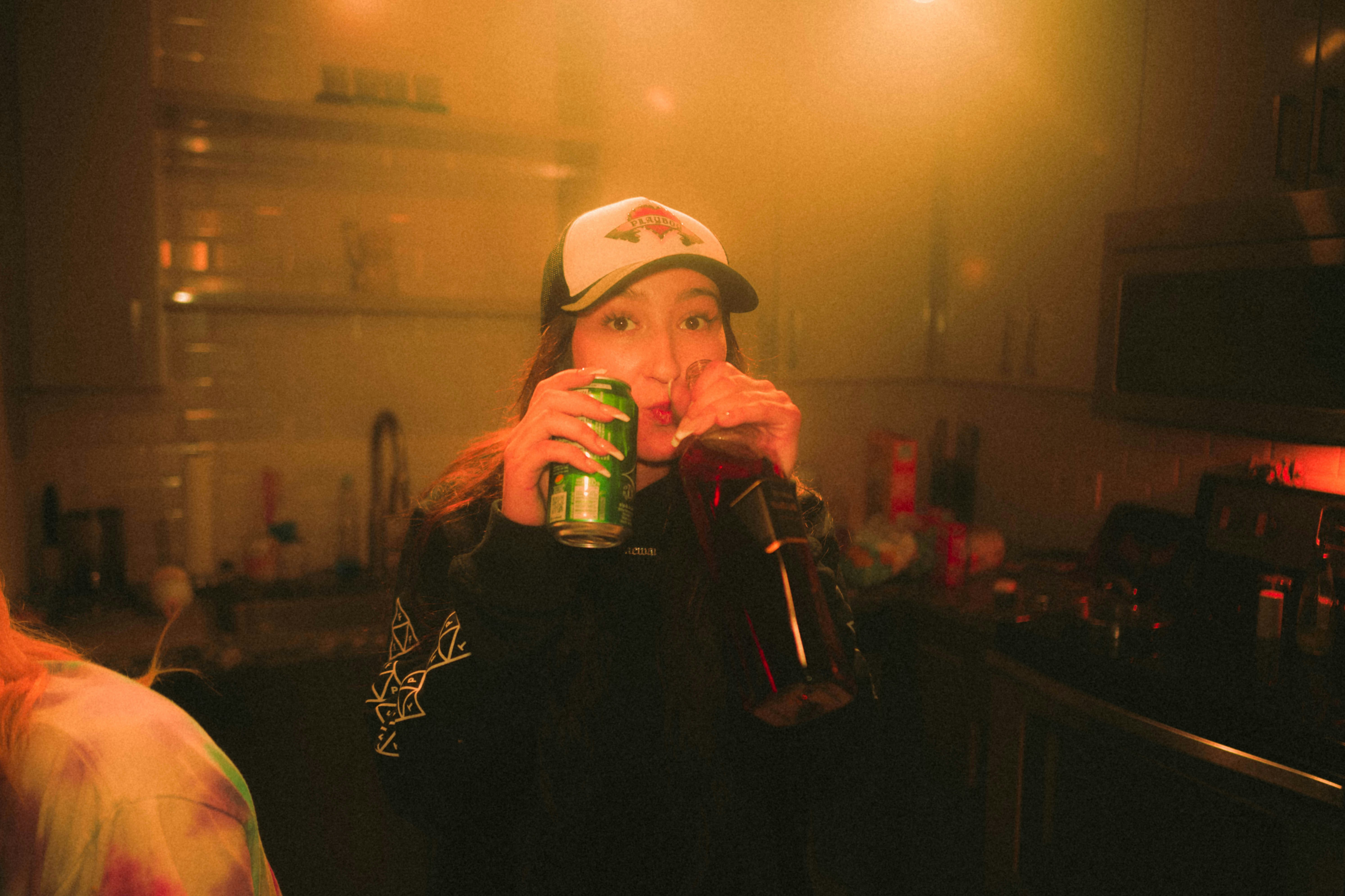 a woman drinking a can of soda in a kitchen