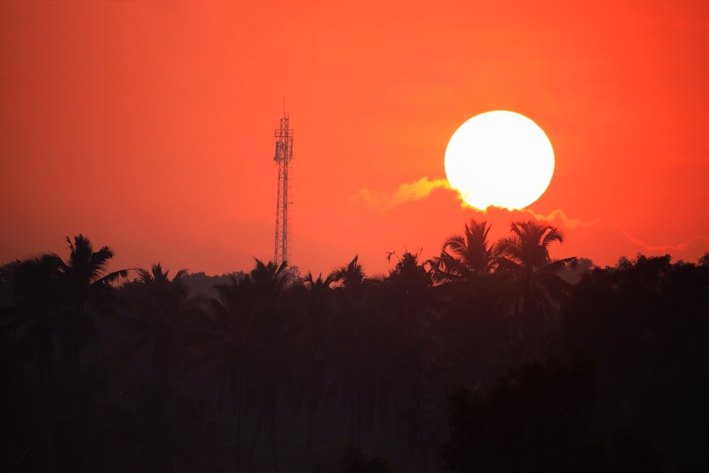 the sun is setting behind a tower in the distance