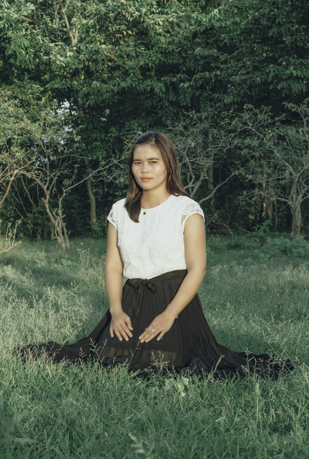 a woman sitting in the grass in front of trees