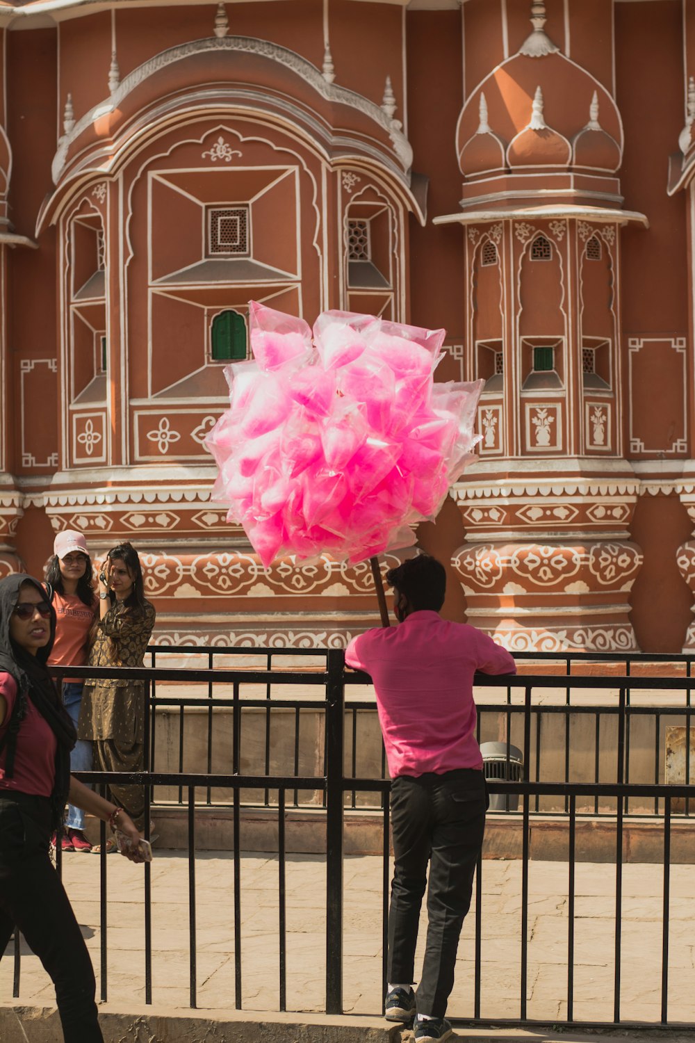 a person holding a pink object in front of a fence