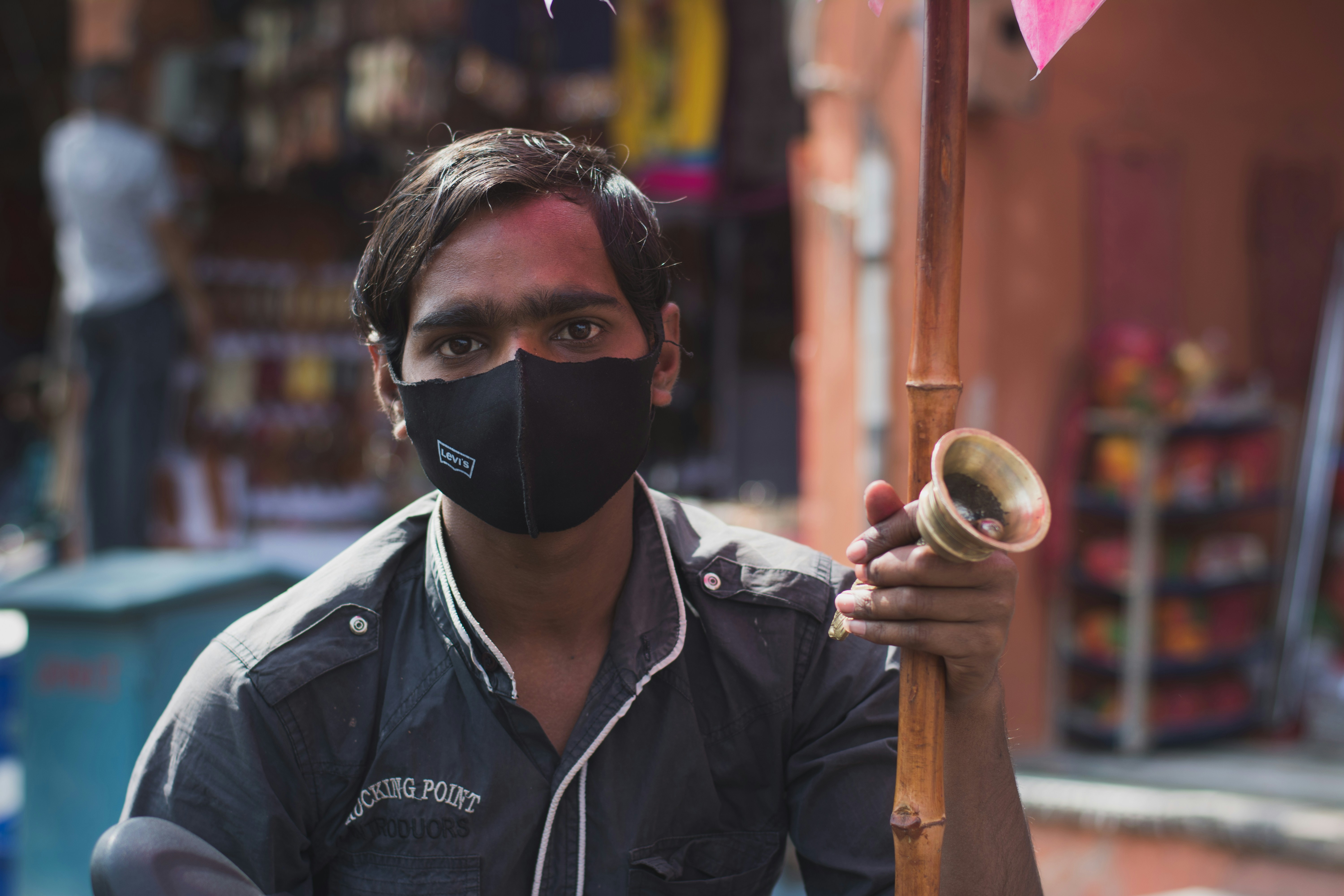 A candy-seller wearing a mask with a bell in his hand selling pink candies on the roads of Jaipur Rajasthan poses for the camera.