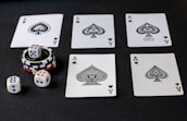 Five playing cards, all aces of spades, are arranged on a dark surface. Beside the cards, there is a stack of poker chips with two dice on top. Three additional dice are placed nearby, with both the poker chips and dice featuring a combination of red, blue, and white colors.