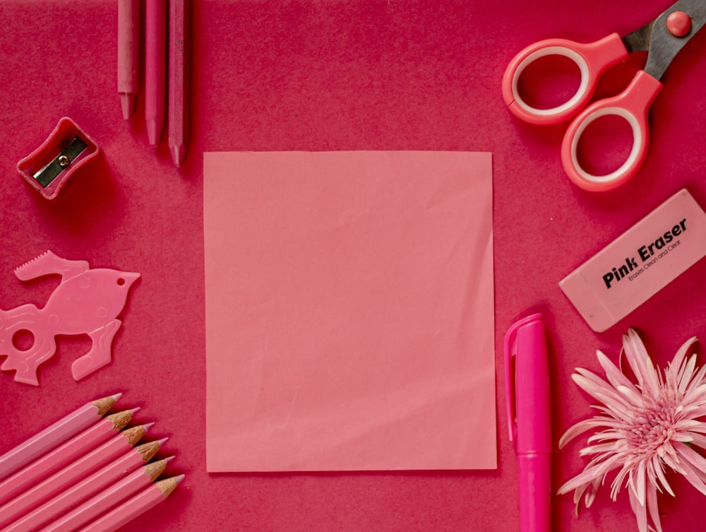 una scrivania rosa con un blocco note, matite, forbici e altri oggetti
