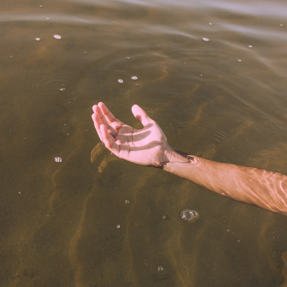 a person's hand reaching for a frisbee in the water