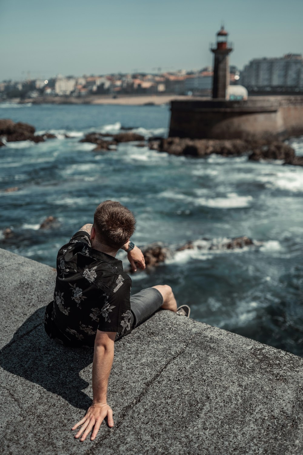 a man sitting on a ledge looking out at the ocean