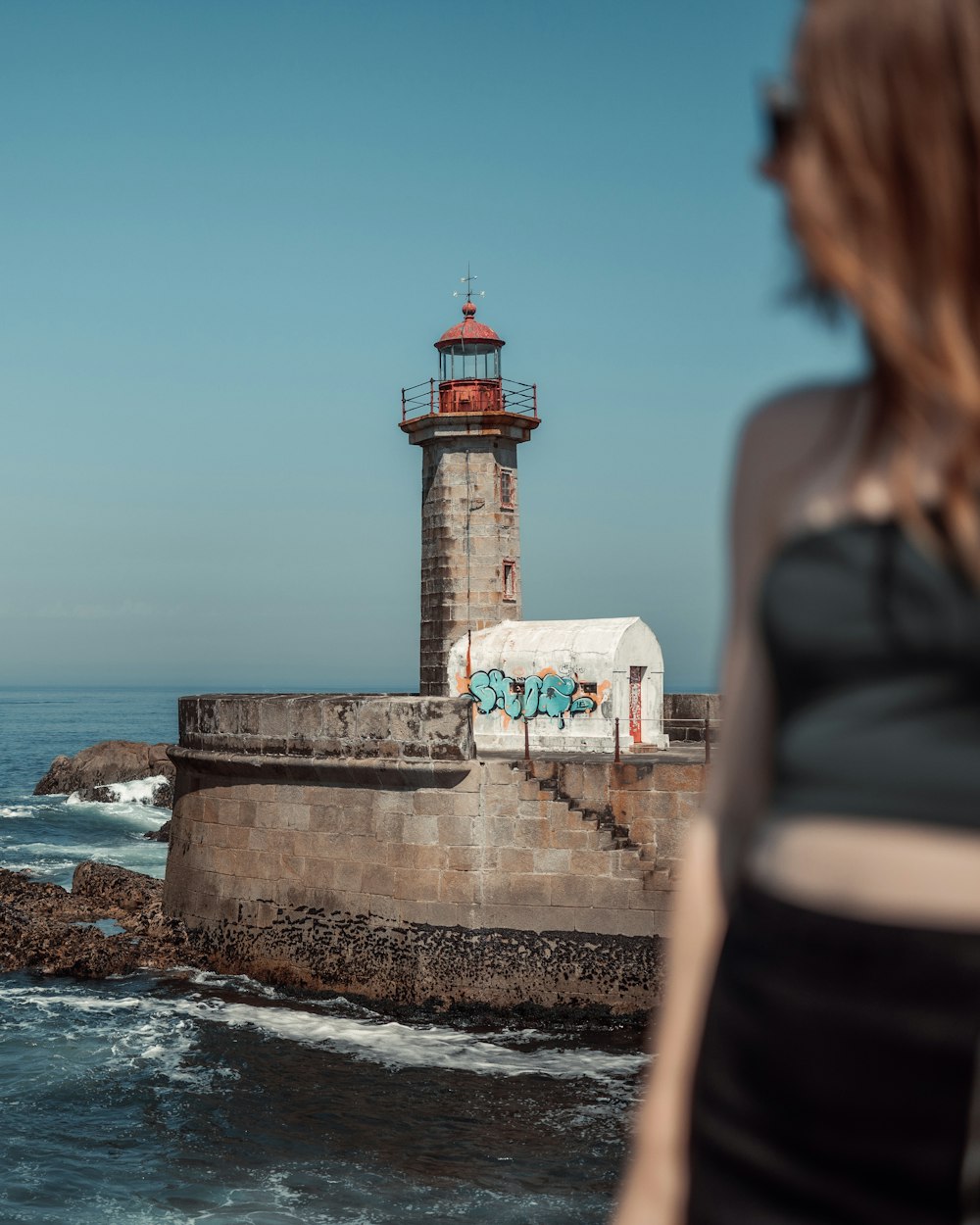 a woman standing next to a light house near the ocean