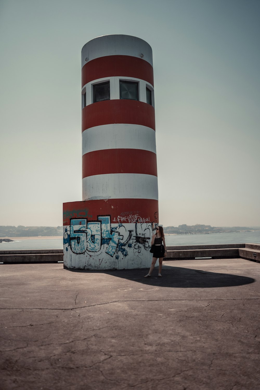a woman standing in front of a red and white lighthouse