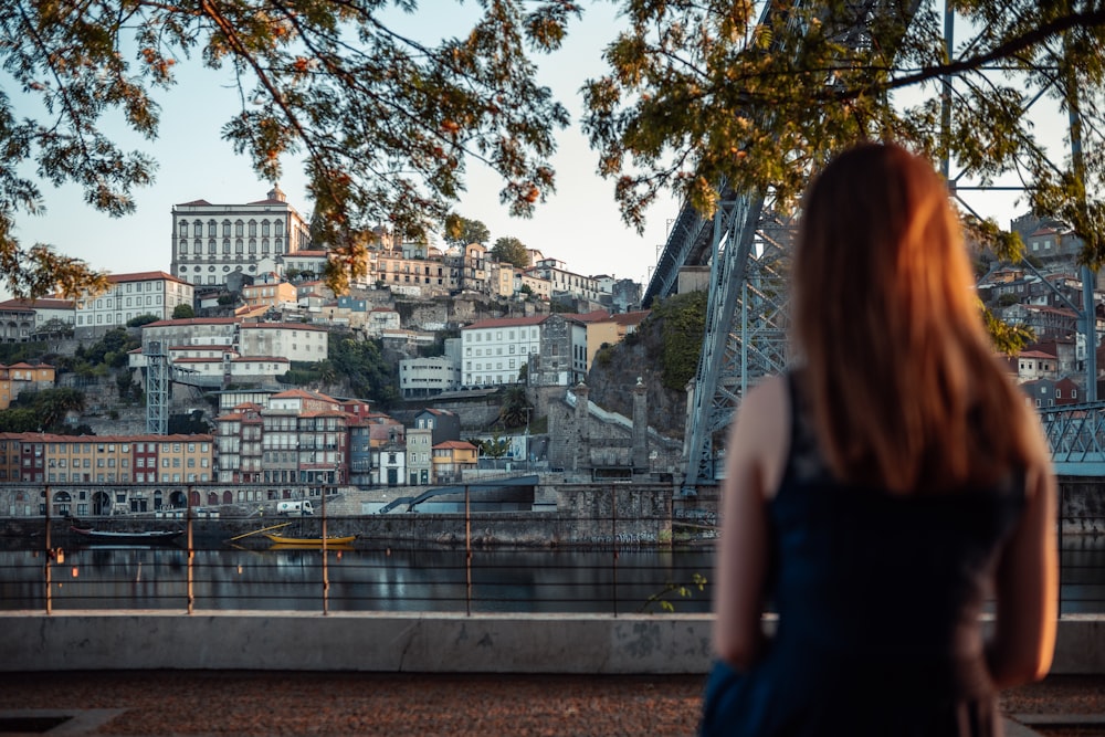 a woman standing on a bridge looking at a city