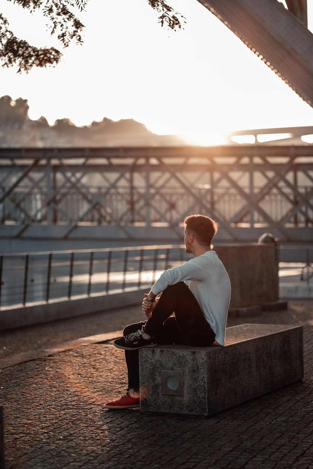 a man sitting on a bench in front of a bridge