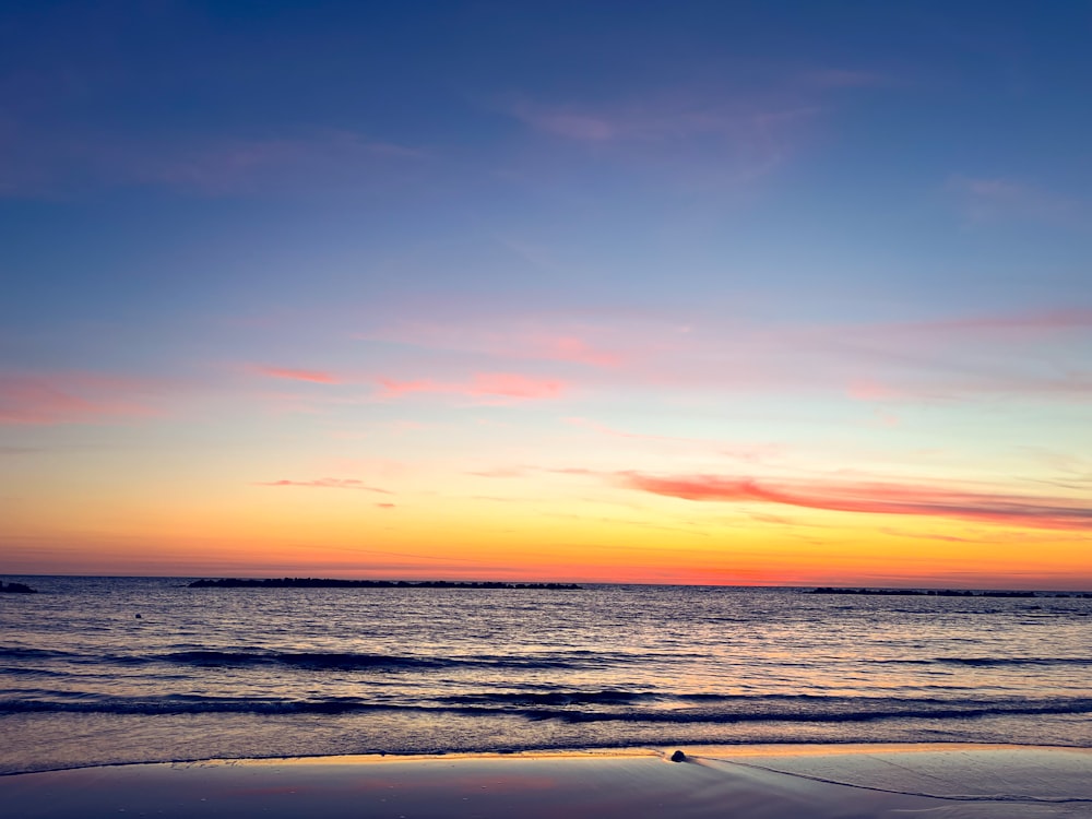 the sun is setting over the ocean on the beach