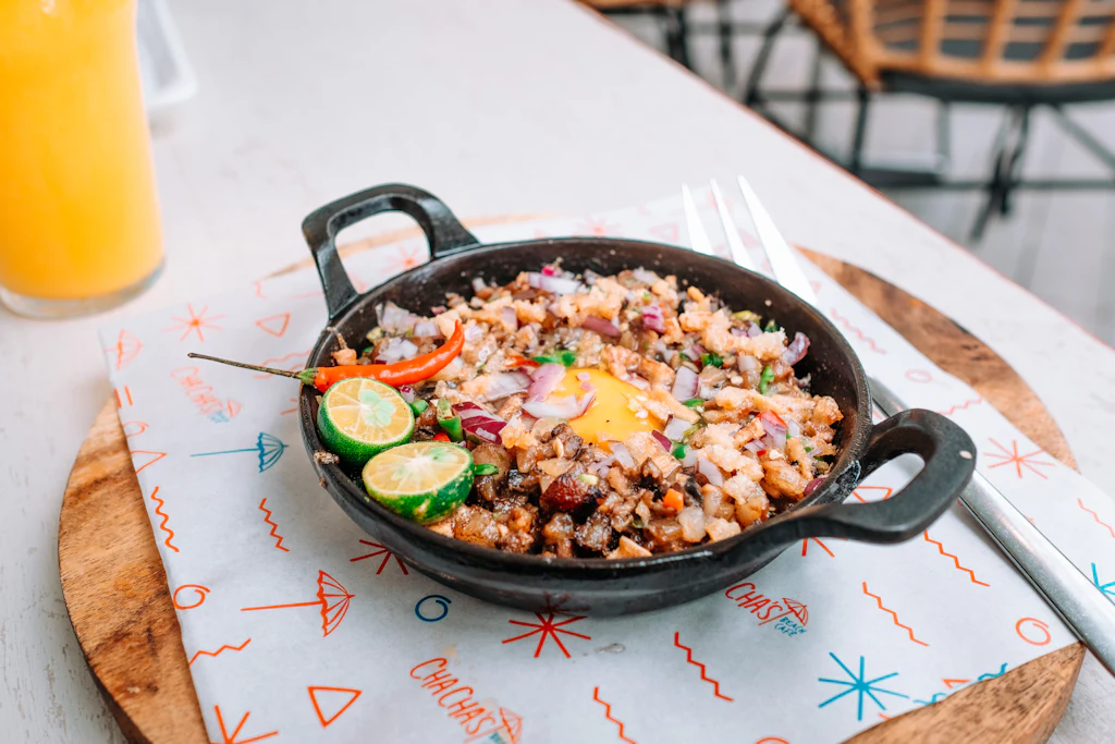 Sizzling pork sisig topped with egg, red onion, chilli and calamansi in a black pan