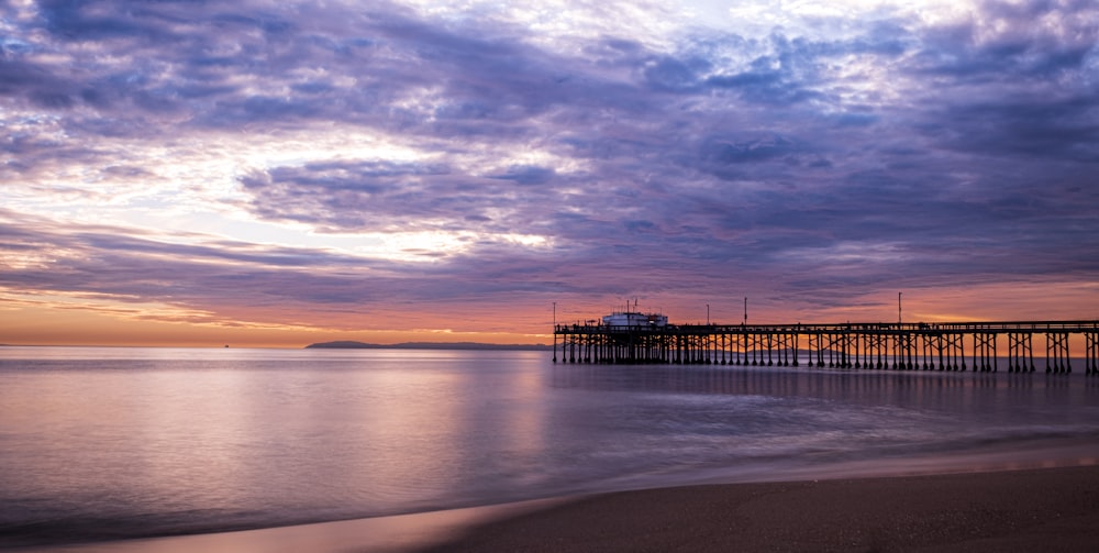 a pier on a beach with a sunset in the background