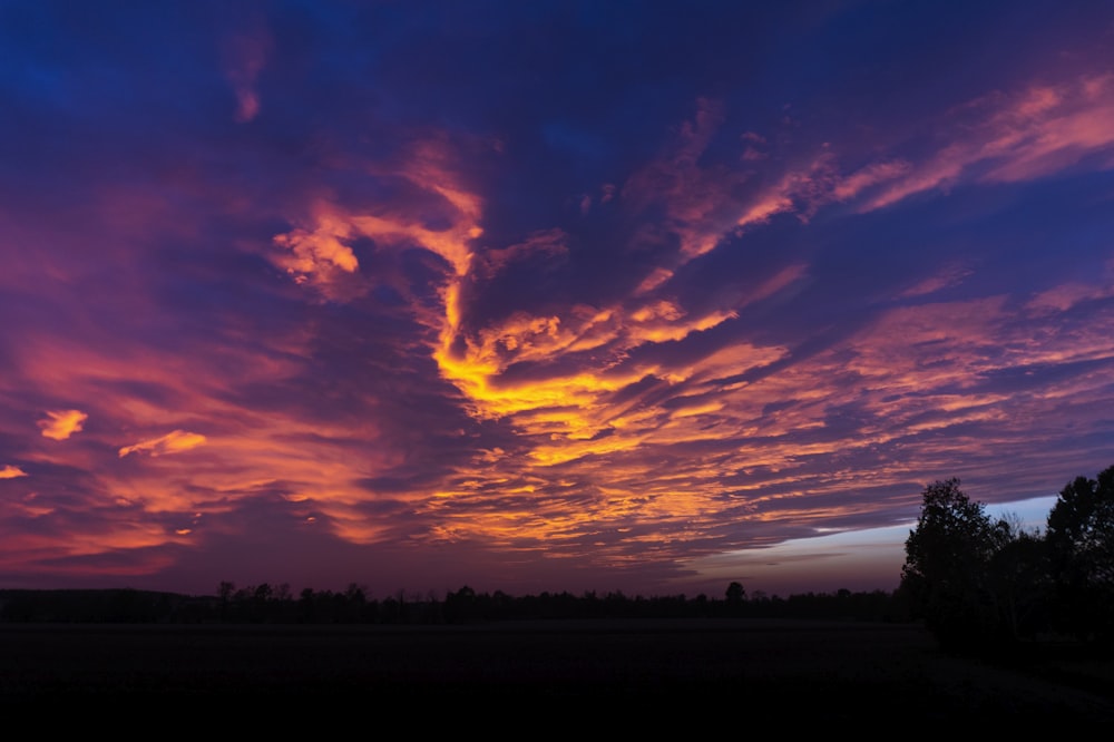 a purple and blue sky with clouds and trees