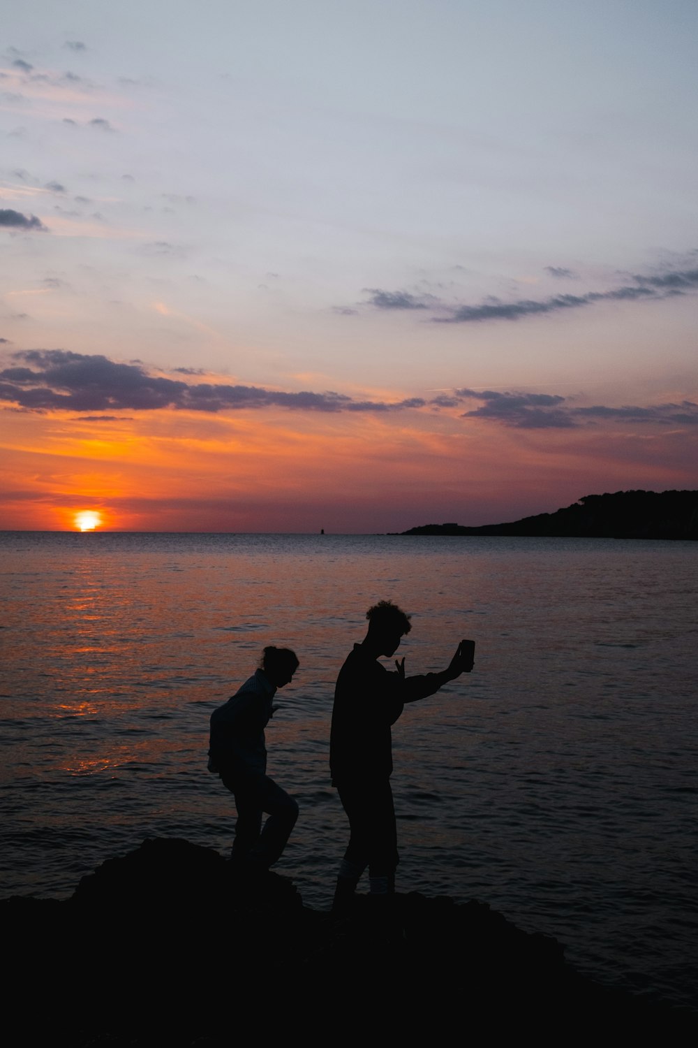 a couple of people standing on top of a rock near the ocean