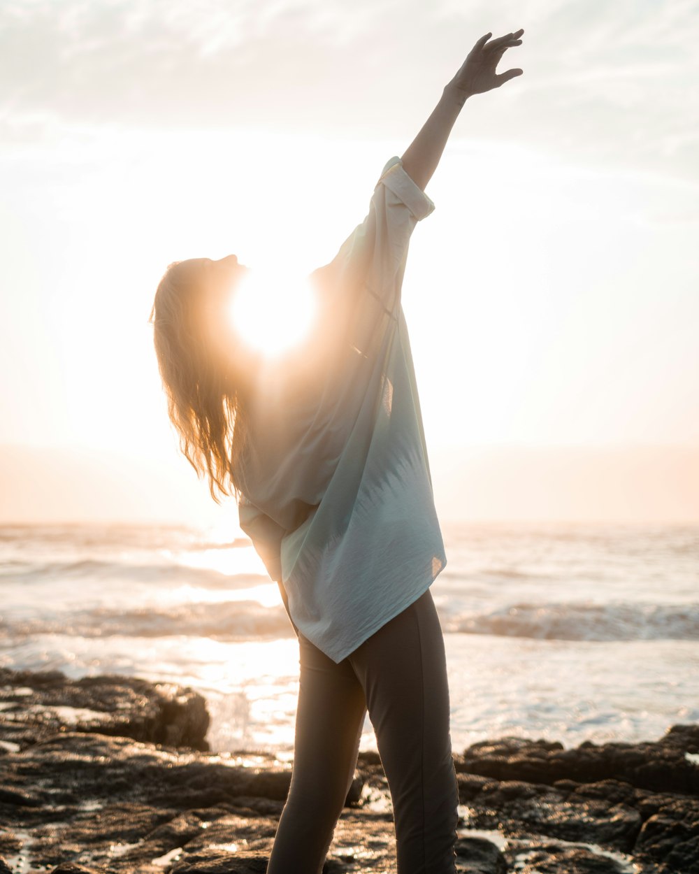 a woman standing on a beach with her arms in the air