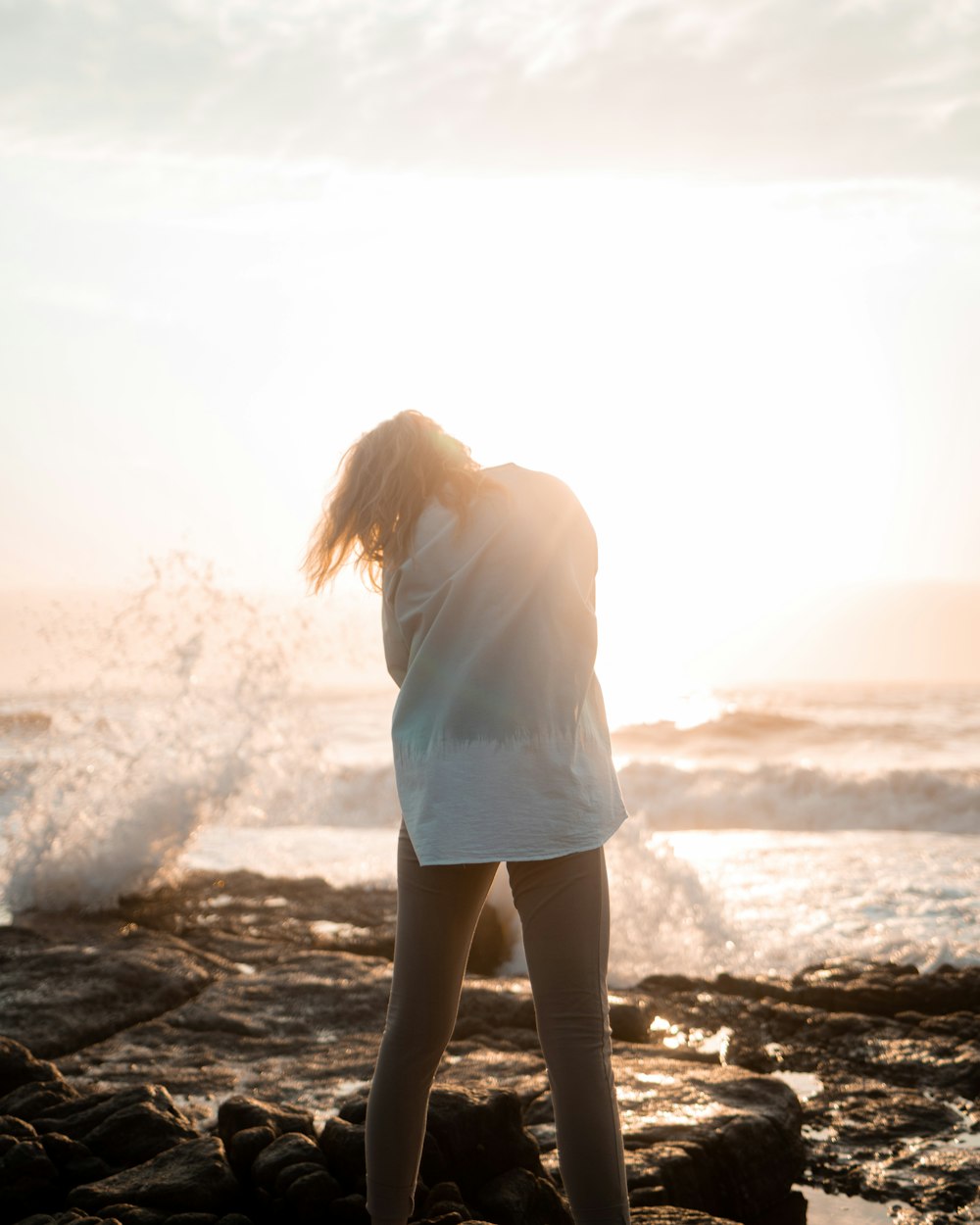 a woman standing on a rocky beach next to the ocean