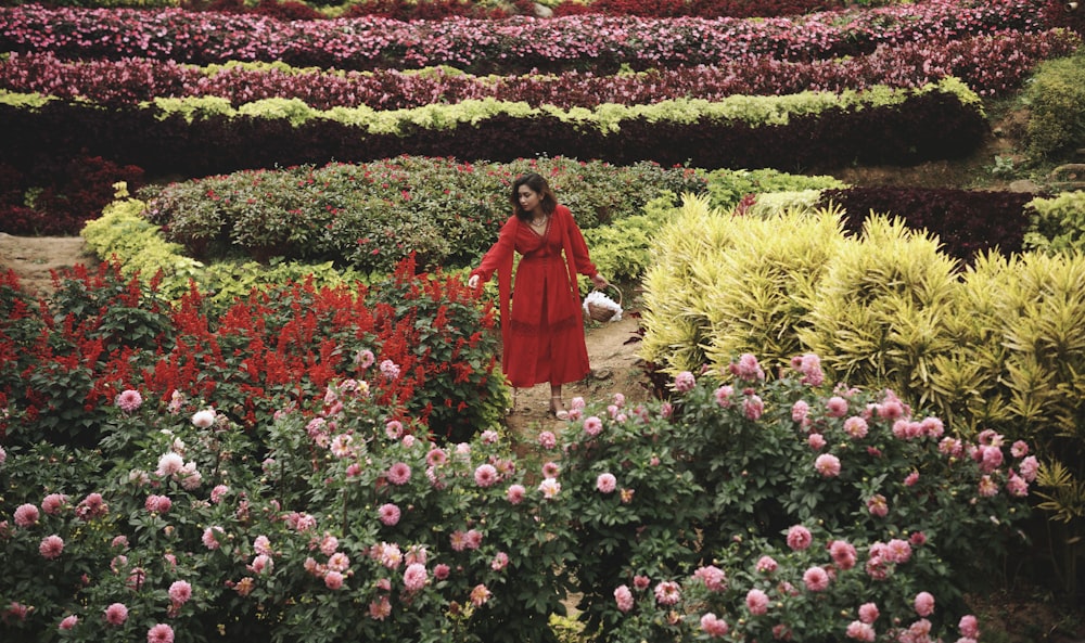 a woman in a red dress walking through a garden