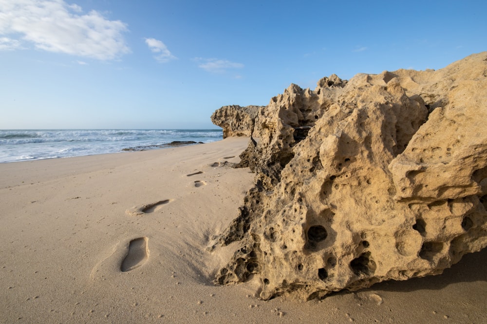 a rock on a beach with footprints in the sand