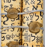 Rolled-up parchment secured with string, featuring various symbols and characters in black ink. The parchment is adorned with gold seals that have designs including a fish symbol and a crown.