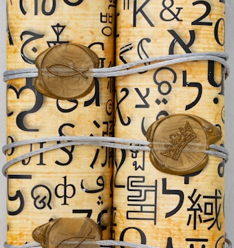 Rolled-up parchment secured with string, featuring various symbols and characters in black ink. The parchment is adorned with gold seals that have designs including a fish symbol and a crown.