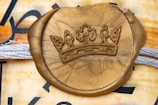 A gold wax seal embossed with a crown emblem is placed over a textured background featuring intertwined white threads. The background includes a mix of muted and warm colors with partial black text visible.