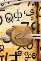 A close-up image of a scroll with various black symbol characters printed on it. The scroll is tied with a white string and features a gold wax seal with a fish symbol embossed on it.
