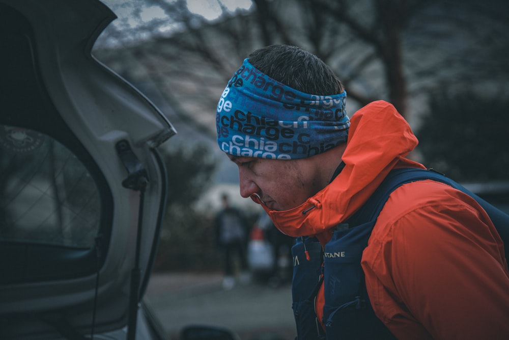 a man wearing a blue and orange headband next to a car