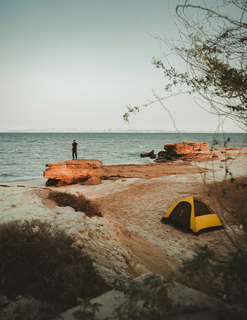 a man standing on a beach next to a tent