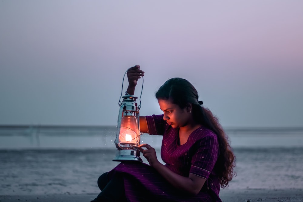 a woman sitting on a beach holding a lantern