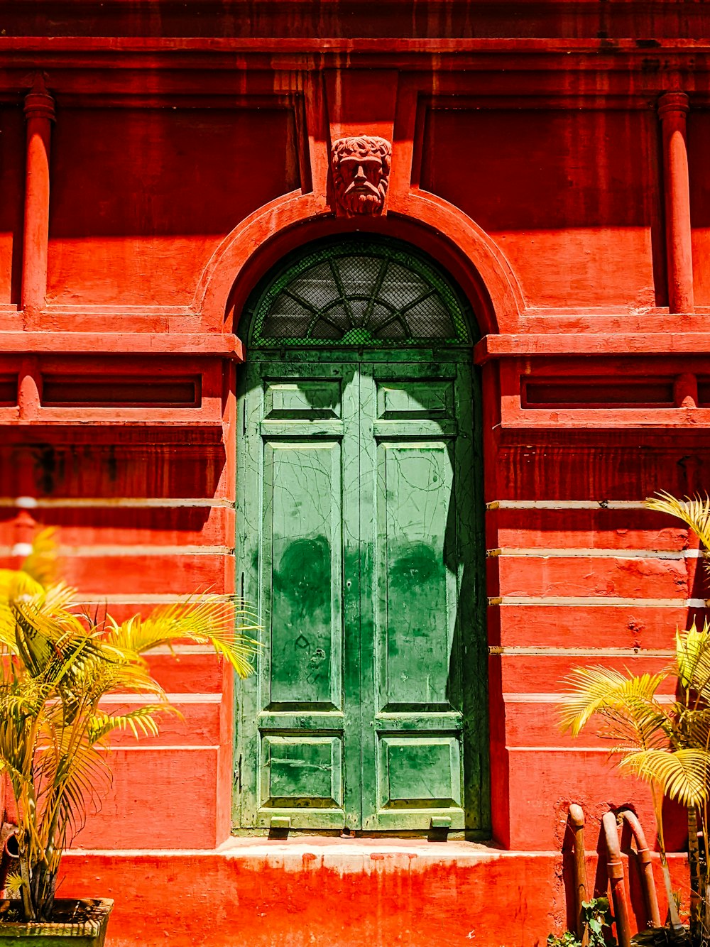 a red building with a green door and two potted plants
