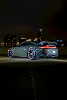 A sleek sports car parked at sunset with vibrant city lights in the background.