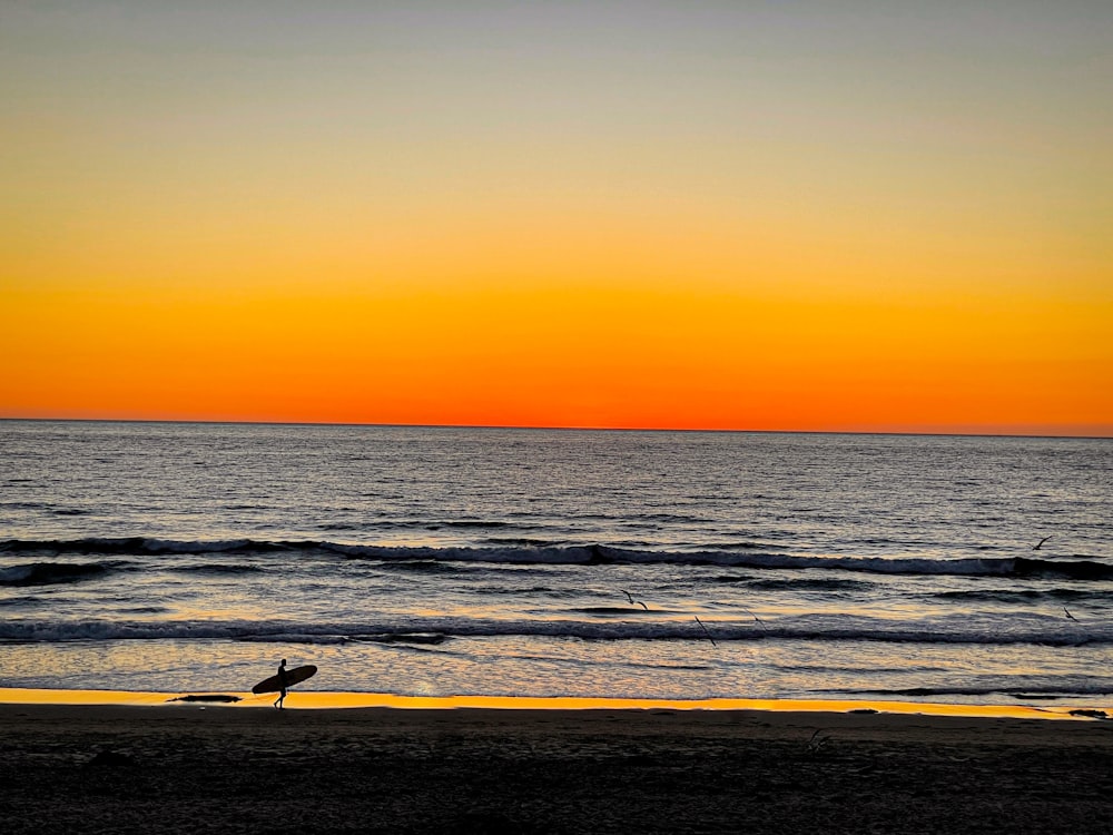 a surfer is walking on the beach at sunset
