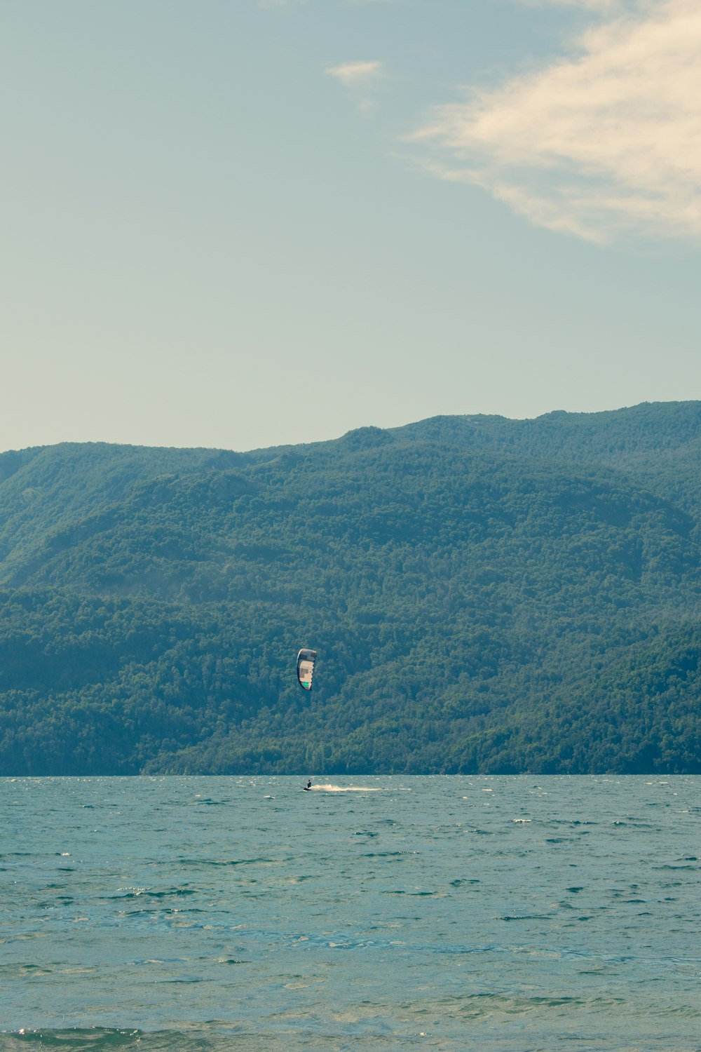 a parasailer glides across the water in front of a mountain range
