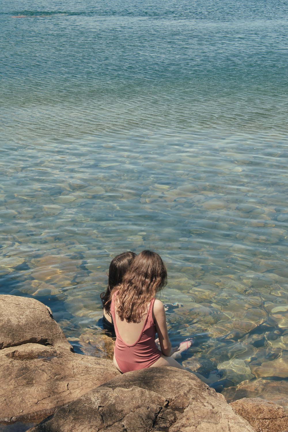 a woman sitting on a rock next to a body of water