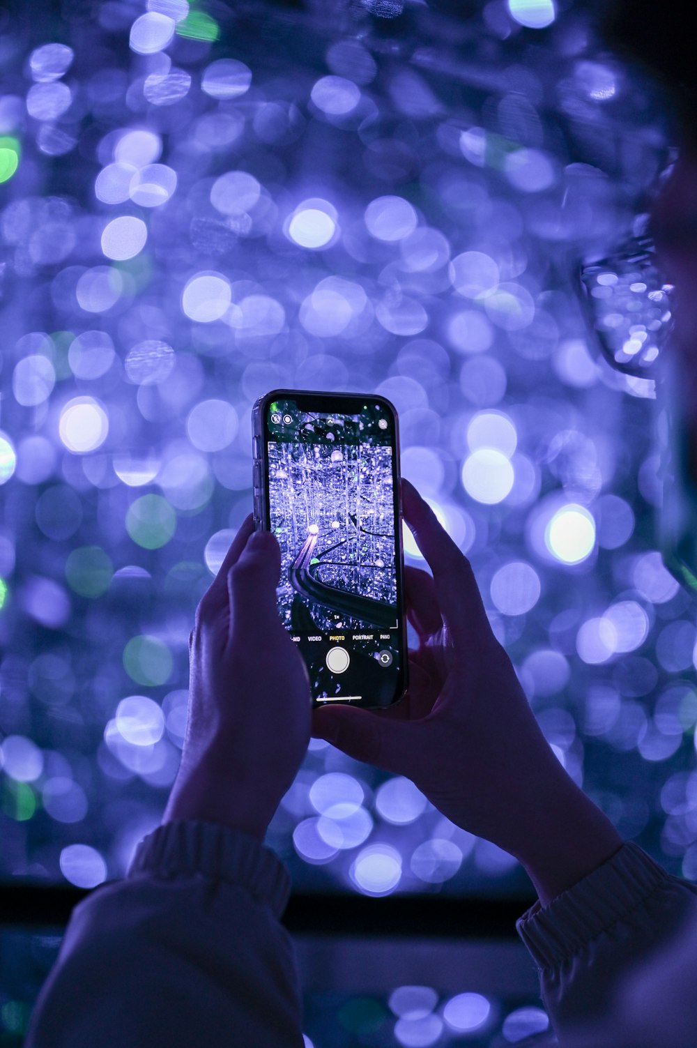 a person holding a cell phone in front of a large display of lights