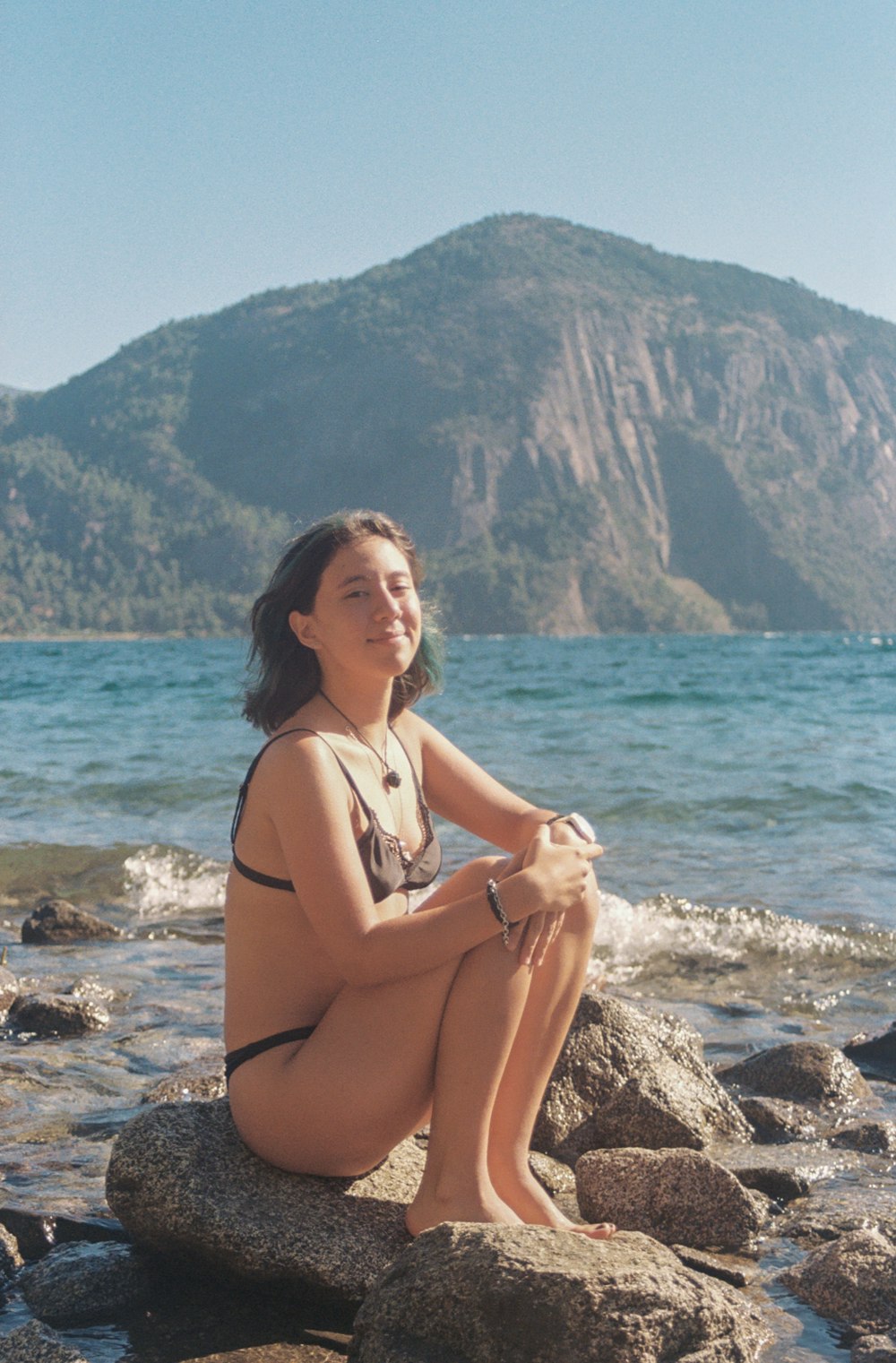 a woman sitting on a rock by the water