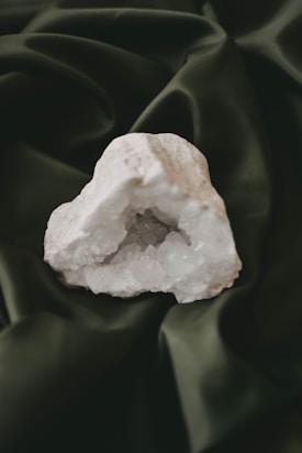 A white geode with sparkling crystals inside rests on a dark green fabric background.