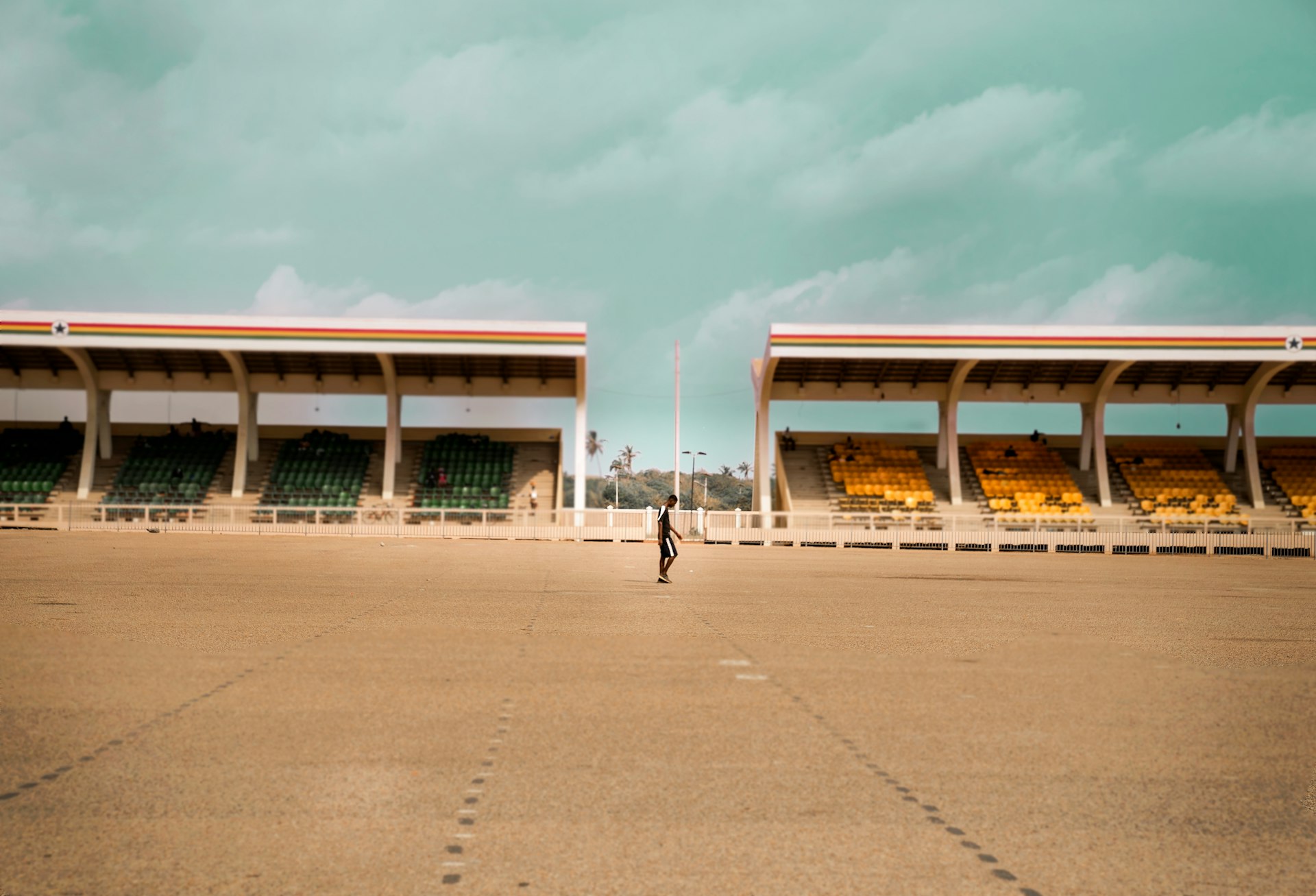 Daily life scene showing a man walking through a parking lot near a stadium in Accra