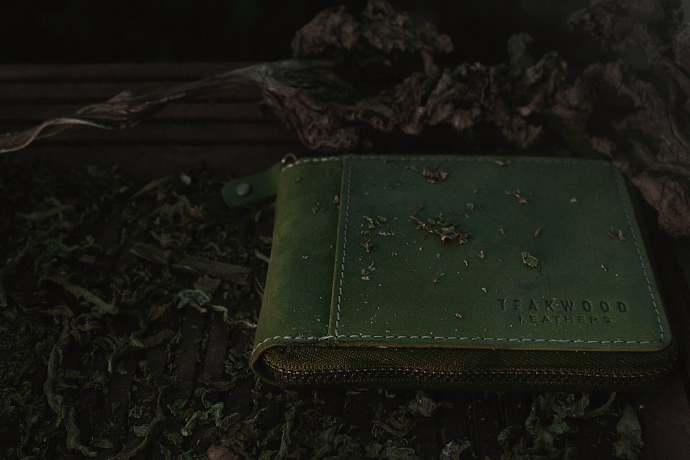 a green leather book sitting on top of a pile of leaves