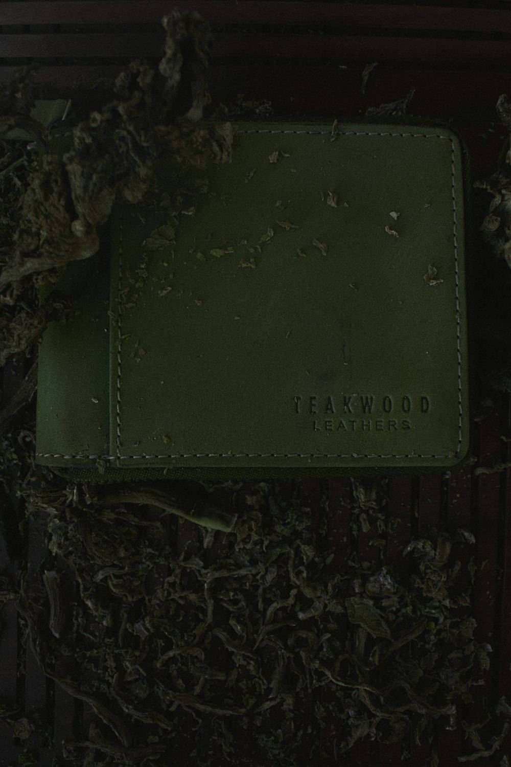 a green leather wallet sitting on top of a pile of leaves