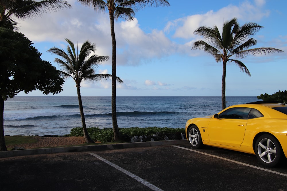 a yellow sports car parked in a parking lot next to the ocean