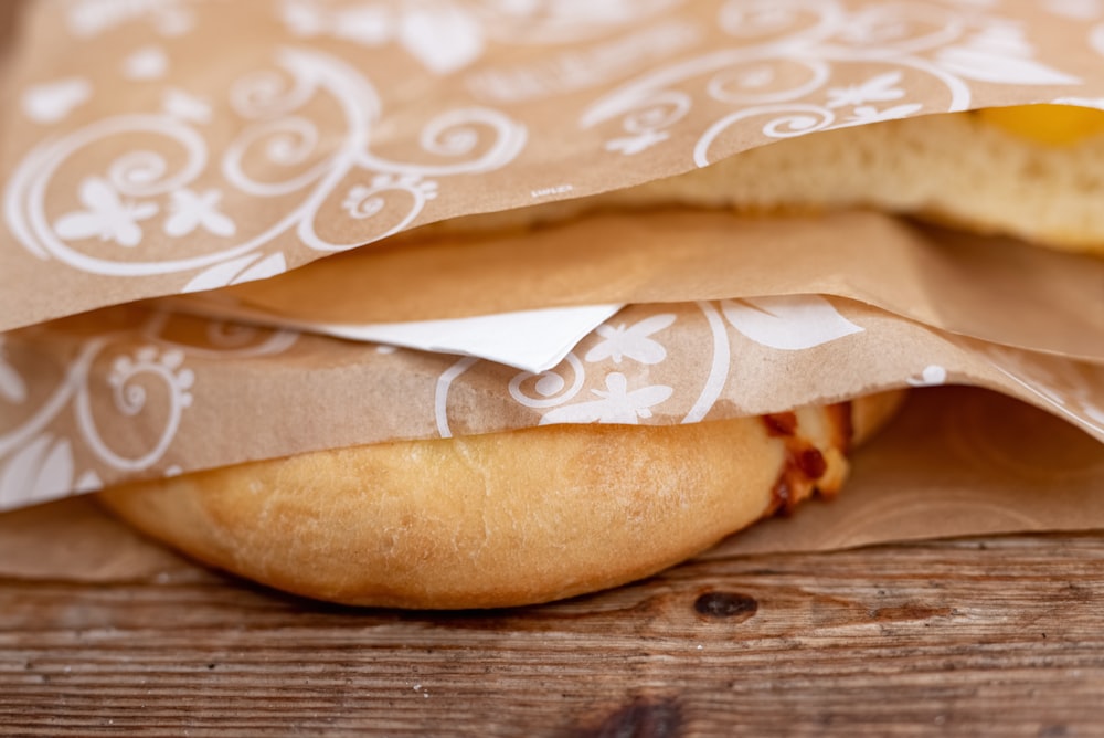 a sandwich wrapped in brown paper on top of a wooden table