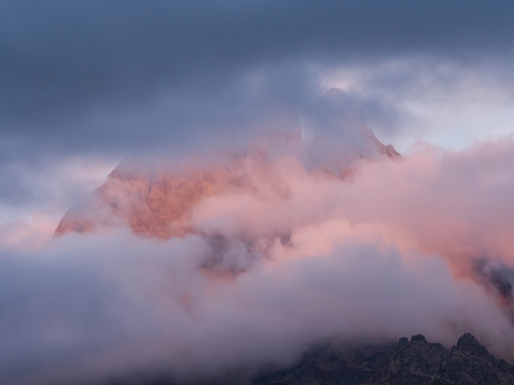 a mountain covered in clouds with a pink sky