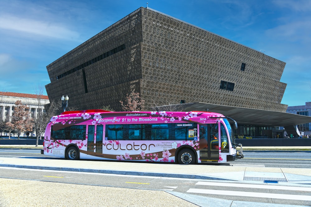 a pink and white bus parked in front of a building