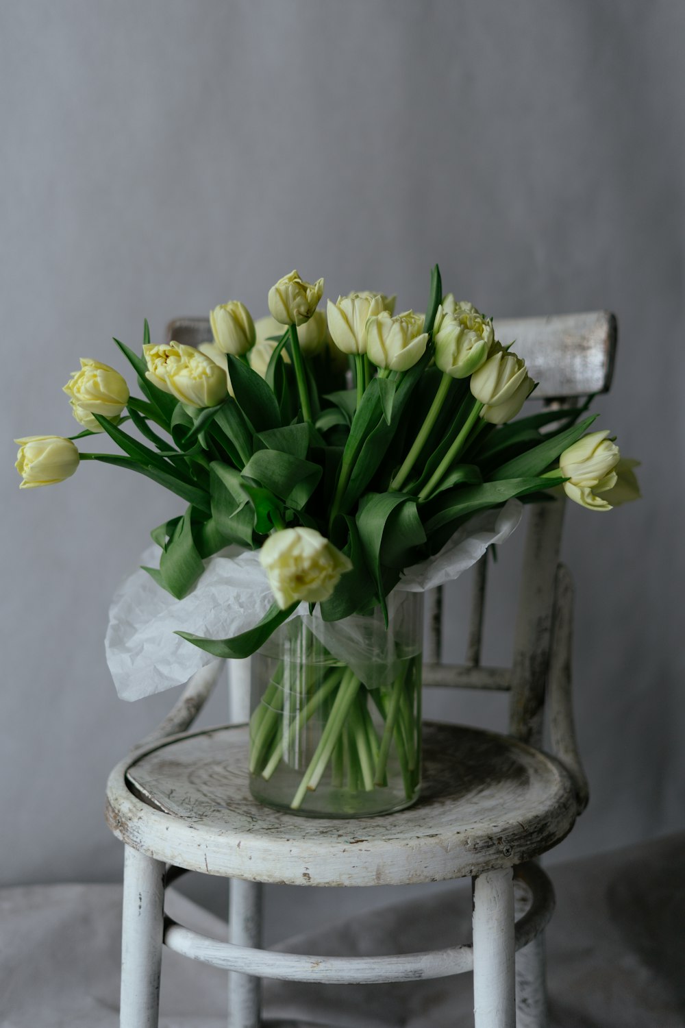 a bouquet of yellow tulips in a vase on a chair