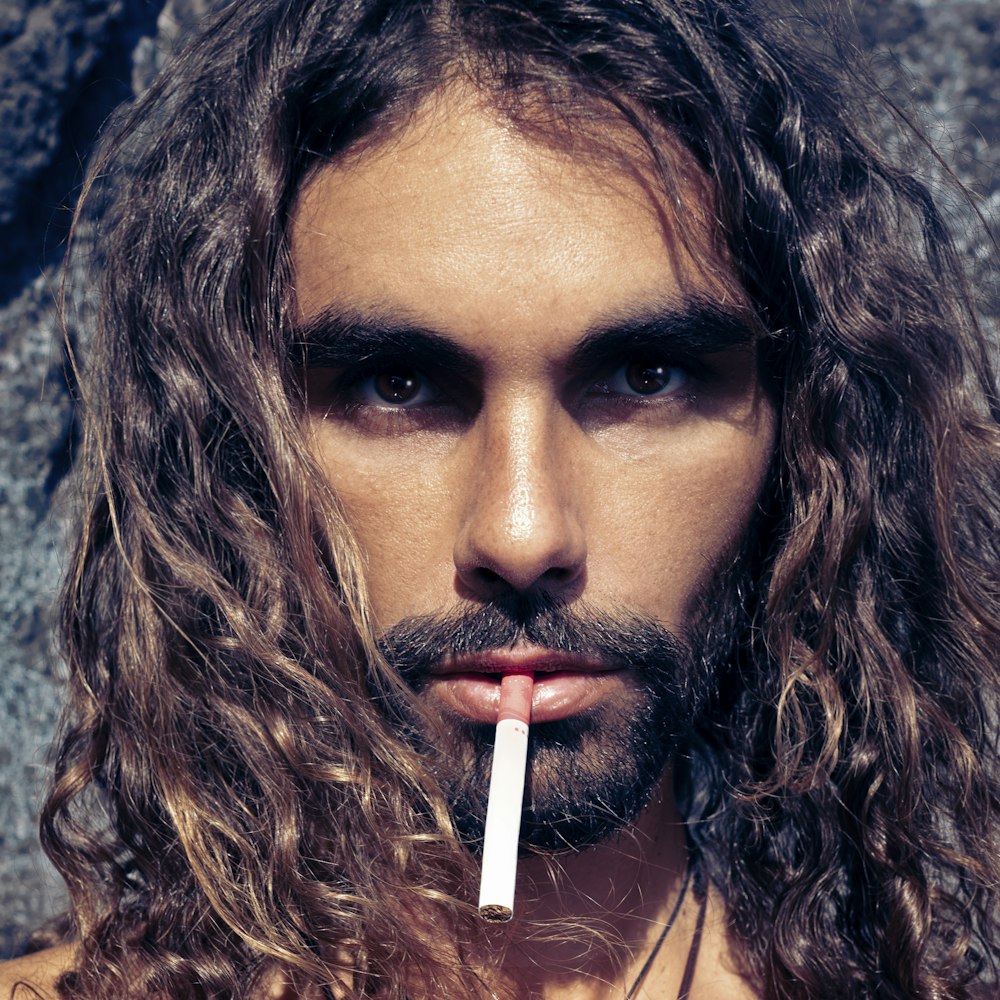 um homem com cabelos compridos e um cigarro na boca