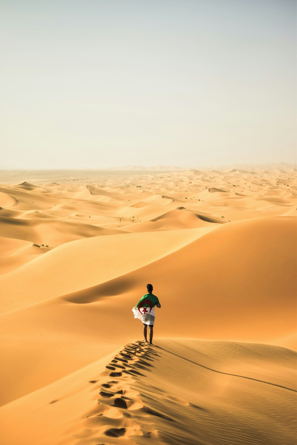 a man walking across a desert holding a surfboard