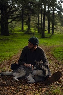 a man sitting on the ground with two dogs